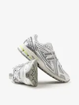 Championes urbanos New Balance modelo 1906R, con diseño técnico en tonos gris, blanco y detalles en verde lima. Presentan una estructura de malla transpirable con superposiciones sintéticas, logo N lateral y entresuela con tecnología de amortiguación.