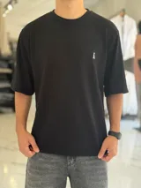 Remera negra de corte oversize y tejido texturizado, con mangas cortas y cuello redondo. Cuenta con un pequeño bordado blanco en el pecho izquierdo.