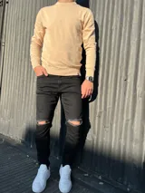 Pantalón chupín de jean color negro, de corte ajustado y diseño con roturas en las rodillas.