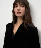 Blazer de terciopelo color negro con largo extendido, diseño cruzado con botones frontales, solapa clásica, bolsillos con tapa y mangas largas.