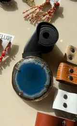 Cinturón de cuero negro con hebilla artesanal de piedra ágata azul rodeada por un marco metálico dorado.