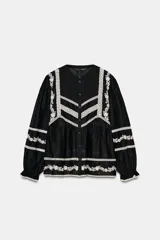 Blusa negra de manga larga con cuello redondo y cierre frontal de botones. Presenta amplios detalles de bordados y encajes blancos en el canesú frontal, mangas y ruedo inferior.