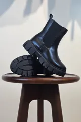 Bota tipo Chelsea de caña corta en color beige, confeccionada en material sintético con acabado liso. Presenta paneles elásticos laterales a tono y una suela track robusta y dentada que aporta altura y estilo moderno.