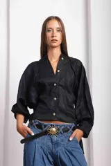 Camisa de lino blanca, de corte oversize, con mangas largas abullonadas, cuello mao y botones. Es más larga en la parte trasera e incluye un tajo en la espalda.