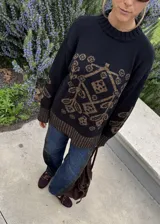 Buzo de punto negro con diseño geométrico y floral en tono marrón, de cuello redondo y manga larga.