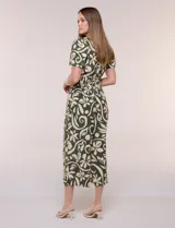 Enterito verde oscuro con estampado floral y abstracto en tono beige, de corte suelto y caída fluida. Presenta escote en V, mangas cortas, cintura elastizada con faja fruncida y pantalón crop de pierna ancha con bolsillos laterales.