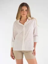 Blusa blanca de broderie, con cuello camisero, cierre frontal con botones y mangas tres cuartos con puños anchos lisos.