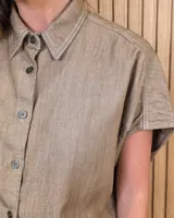 Camisa de manga corta color beige, de corte holgado, con cuello camisero y cierre frontal de botones.