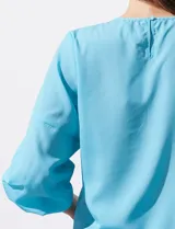 Blusa de gasa con estampado geométrico en tonos negro, gris y celeste. Tiene cuello redondo y mangas 3/4 amplias con abertura y botón.