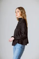 Blusa negra de manga larga con cuello alto fruncido y diseño amplio con frunces en la parte superior.