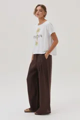 Remera blanca de algodón con cuello bote y manga corta, con un estampado central que incluye dos palmeras reflejadas y la palabra "SUNRISE" bordada en el centro.