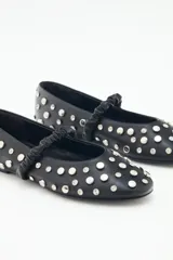 Balerinas de cuero negras con remaches de níquel y piedras símil cristal. Tienen una tira elástica fruncida sobre el empeine para ajuste y suela de goma con plantilla acolchonada.