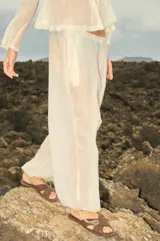 Pantalón de organza color crudo, de corte holgado y diseño traslúcido. Presenta cintura elástica con cordón ajustable y terminaciones en los tobillos con tancas metálicas.