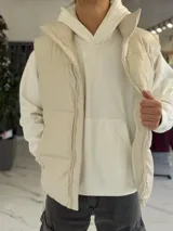 Chaleco puffer de cuerina beige, sin mangas, con cuello alto, cierre frontal y bolsillos laterales.