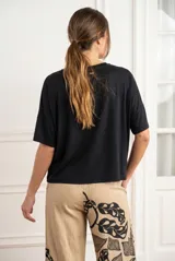 Remera negra de corte oversize, con cuello redondo y mangas cortas de caída fluida. Presenta un diseño minimalista con aberturas laterales en el ruedo.
