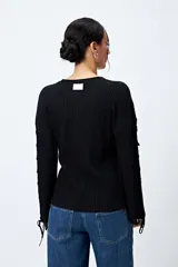 Sweater color crema de tejido de canalé con detalle de trenzado en las mangas y terminación con lazo ajustable.