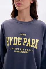 Buzo oversize azul con cuello redondo y estampado frontal en amarillo que dice "London Hyde Park Around The World Global Dreamers".