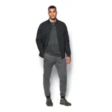 Pantalón deportivo tipo jogger para hombre, color gris jaspeado, con cintura elástica negra y cordón de ajuste. Presenta puños ajustados en los tobillos y un bolsillo lateral con cierre. Logo de Under Armour bordado en la pierna izquierda.
