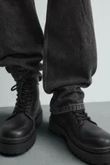 Bota tipo derby con cordones, confeccionada en material liso con horma redonda. Presenta una suela con volumen y piso track dentado.