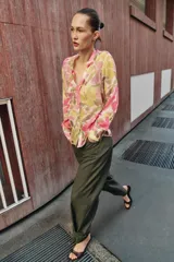 Blusa de manga larga con estampado floral en tonos rosados, verdes y beige. Presenta escote en pico con detalle de abalorios colgantes y cierre frontal con botones.