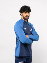 Buzo de entrenamiento Umbro del Club Nacional de Football, con medio cierre frontal, cuello alto y mangas largas. Presenta el logo de la marca y el escudo del club en el pecho.