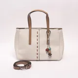 Cartera tipo tote de color blanco con detalles en tostado, asas de mano y correa larga ajustable y extraíble. Cuenta con costuras decorativas y un llavero colgante con cuentas de colores.