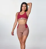 Conjunto deportivo de dos piezas compuesto por un top y un short de tiro alto. El top es de estilo deportivo con doble bretel y diseño bicolor en tonos bordó y marrón, con el logo 'bk.' estampado en el frente. El short es de corte ajustado, con diseño acanalado y paneles laterales en contraste de color bordó.