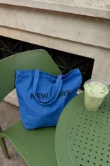 Tote bag de tela azul con estampado de la inscripción 'New York' en negro, diseño amplio con doble asa de hombro.