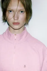 Sudadera de algodón color rosado con cuello alto, cierre frontal con cremallera metálica y manga larga. Presenta aplicación metálica en el pecho y acabados en rib.