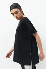 Remera oversized de algodón color negro, con cuello a la base y mangas cortas con puños doblados. Presenta una abertura lateral con botones de tachas plateados.