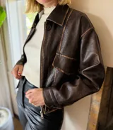 Campera de eco cuero en tono marrón con efecto desgastado, corte oversize y cierre frontal. Presenta costuras marcadas, bolsillos frontales y puños con botones.