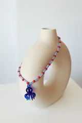 Collar corto con cuentas de plástico amarillas y verdes, y dije de vidrio con forma de pulpo negro.