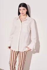 Camisa blanca oversize de algodón, con cuello clásico, cierre frontal con botones de nácar y bolsillo en el pecho.