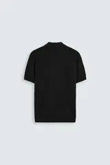 Polo de punto negro, manga corta, con cuello solapa y cierre frontal de tres botones. Presenta un calce regular y acabados en rib en mangas y ruedo.