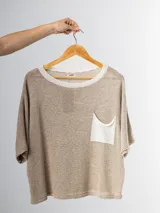 Remera tejida color crema con cuello redondo y bolsillo frontal verde.