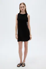 Vestido corto negro sin mangas, con cuello redondo y detalles de volados en las sisas.