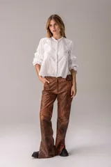 Blusa blanca de broderie con cuello alto con volados, mangas largas abullonadas con detalles de encaje y pliegues decorativos en el frente.