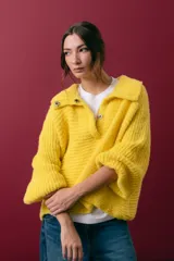 Buzo tejido en mohair de color gris, con silueta amplia y corte en línea A. Presenta cuello tipo remera con broches que permiten cerrarlo como polera, mangas largas con puños y un diseño de tejido horizontal.