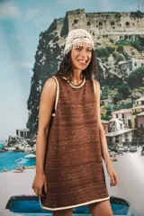 Vestido corto sin mangas, color marrón con hilos dorados entretejidos, creando un efecto texturizado con líneas horizontales caladas. Los bordes del cuello y las sisas son de color crema/beige.