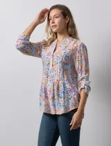 Blusa de gasa estampada con flores en tonos rosa, amarillo y azul. Tiene cuello a la base, escote en V y botones. La delantera tiene detalle plisado y las mangas son 3/4 regulables con presilla y botón.