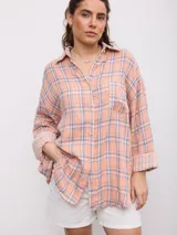 Camisa oversize de manga larga con estampa a cuadros en tonos salmón, gris y blanco, cuello camisero, cierre frontal con botones y bolsillo aplicado en el pecho.