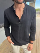 Camisa de manga larga confeccionada en muselina de algodón, color negro. Presenta cuello mao con tapeta frontal de cuatro botones de madera y corte ajustado al cuerpo.