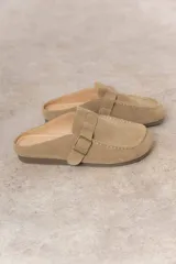 Zueco de cuero gamuzado color marrón, con diseño minimalista y elegante. Cuenta con una tira lateral con hebilla metálica regulable y plantilla acolchada. Su base es liviana y flexible.