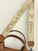 Cartera marrón de cuero genuino con doble asa corta y correa bandolera estampada con la frase "Chabas, soy real, no perfecta".