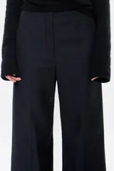 Pantalón largo negro de denim, corte amplio, con cierre frontal con corchete oculto y cremallera, y bolsillos laterales. Contiene 20% de fibras recicladas.