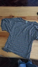 Remera de manga corta gris con rayas horizontales doradas y brillo, ajustada en la cintura con frunce regulable en el lado derecho.