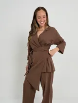 Conjunto de dos piezas confeccionado en lino color beige, compuesto por un pantalón de corte recto y un blazer cruzado con lazo ajustable en la cintura y escote en V.