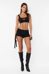 Top negro de gabardina elastizada, con escote recto y breteles anchos. Presenta cordones cruzados con ojalillos metálicos en el centro del pecho y cierre metálico en la espalda.