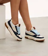 Championes casuales de estilo urbano con diseño de paneles en colores azul marino, beige y celeste. Presentan suela tipo caja de goma color crema con base marrón, cordones gruesos en color celeste y lengüeta acolchada.