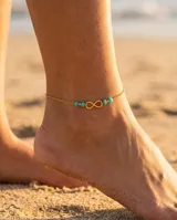 Tobillera de cadena fina de acero con baño de oro, con dije central de símbolo de infinito y cuentas de piedra turquesa.